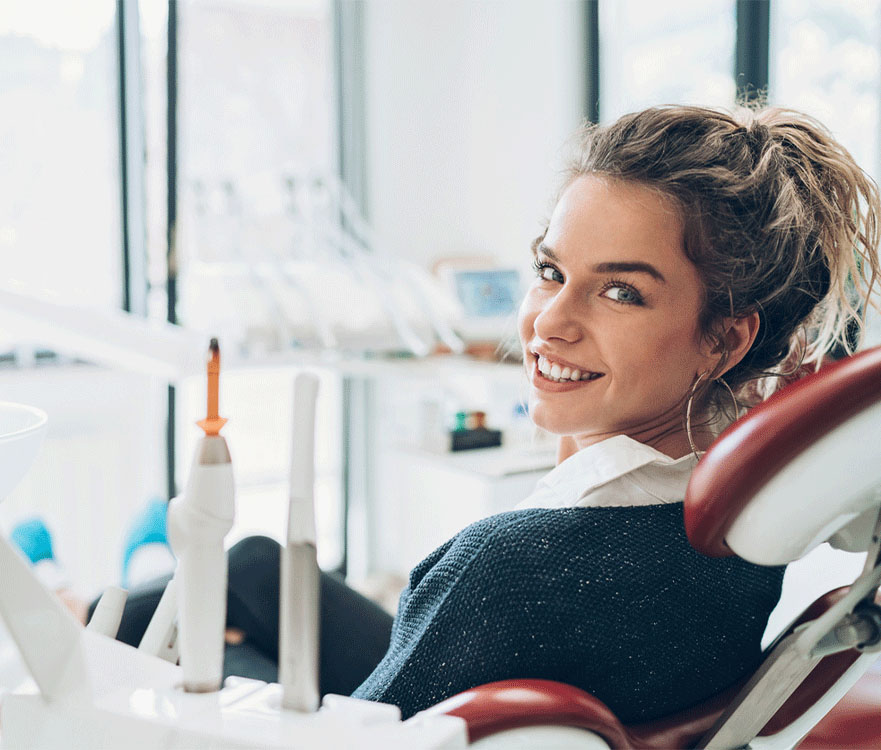 The image shows a woman sitting in a dental chair, likely at a dental clinic. The dental chair is equipped with various dental instruments, including a dental drill and other tools.