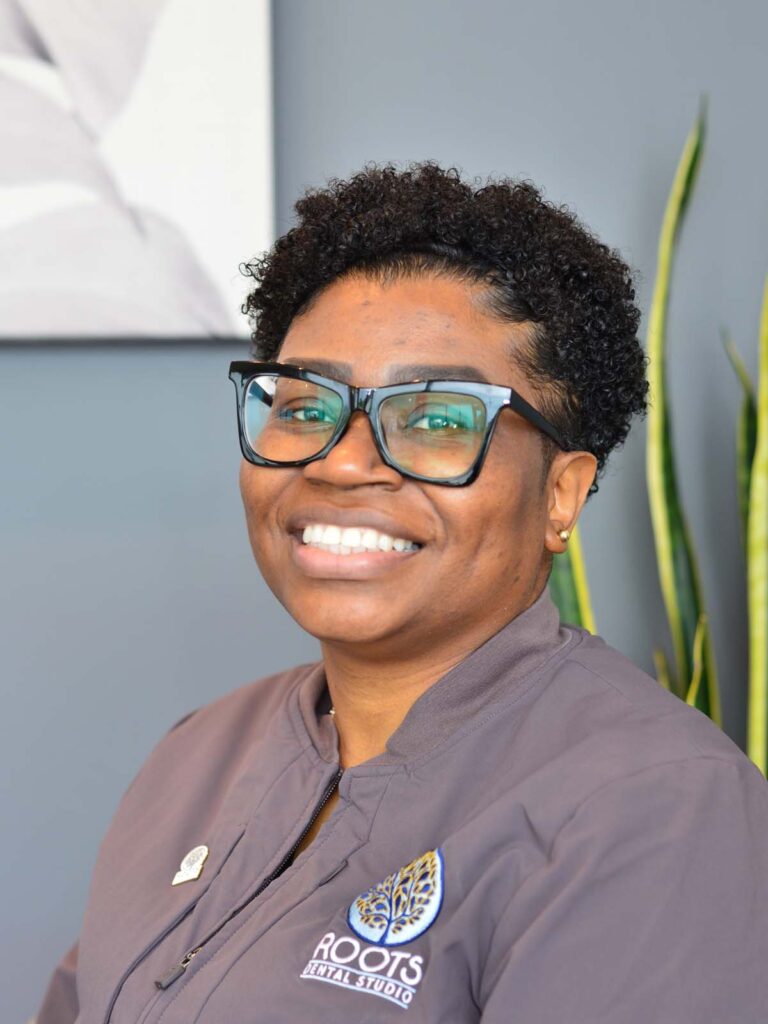 An image of a girl with black curly short hair in a semi side view pose. She's wearing a black eyeglasses and a dark gray uniform.