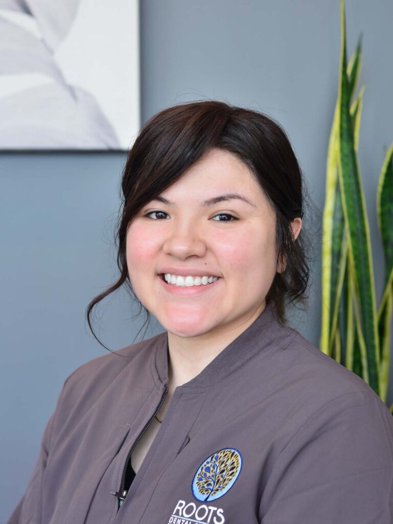 An image of a girl smiling in a semi side view pose. She is wearing a dark gray uniform with a text of "ROOTS" under the logo, that placed on the right side.